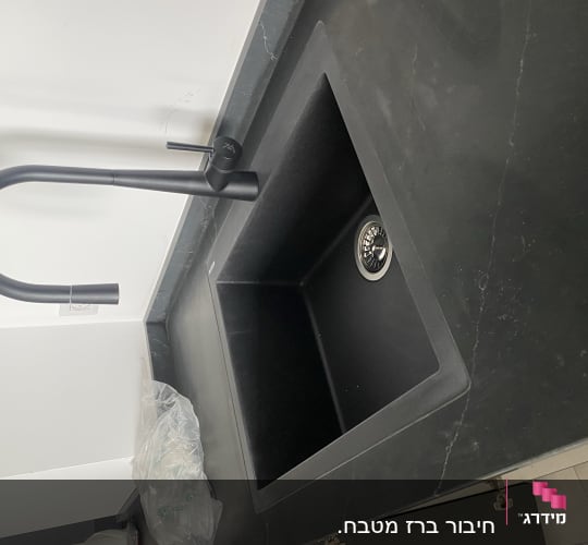 כיור שחור עם ברז מעוקל על משטח עבודה